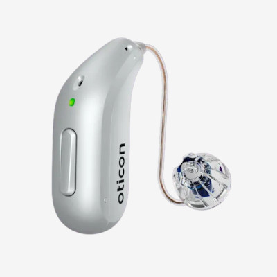 A silver Oticon hearing aid with a green indicator light, a side button, and a clear, dome-shaped earpiece connected by a thin wire.